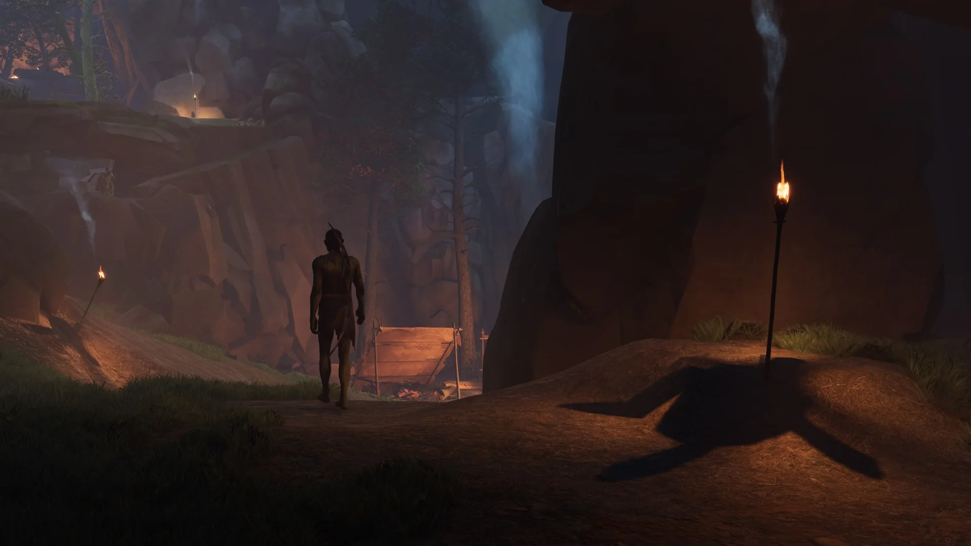 A hunter walks a torch-lit canyon toward a distant campfire beneath towering rock